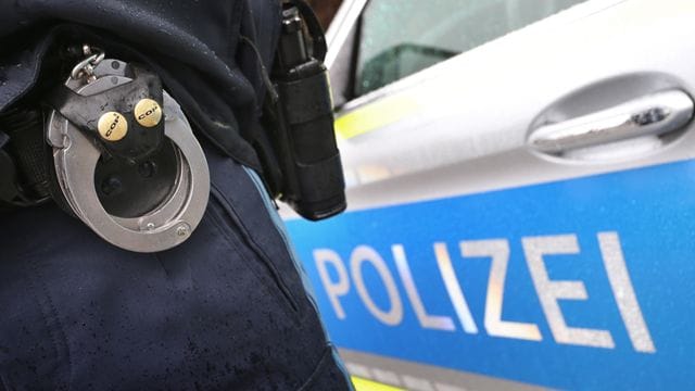 Ein Polizist mit Handschellen und einer Pistole am Gürtel steht vor einem Streifenwagen (Symbolbild): Die beiden Männer wurden vorläufig festgenommen.