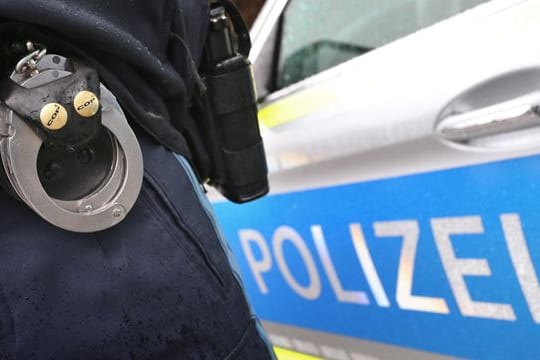 Ein Polizist mit Handschellen und einer Pistole am Gürtel steht vor einem Streifenwagen (Symbolbild): Die beiden Männer wurden vorläufig festgenommen.