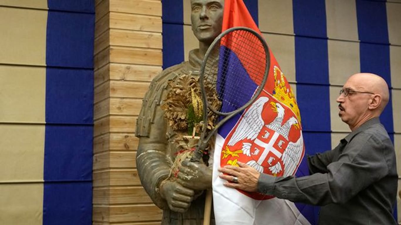 Ein Mann drapiert die serbische Flagge um eine Statue des Tennisspielers Djokovic vor einer Pressekonferenz der Familie des Weltranglistenersten.