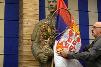 Ein Mann drapiert die serbische Flagge um eine Statue des Tennisspielers Djokovic vor einer Pressekonferenz der Familie des Weltranglistenersten.