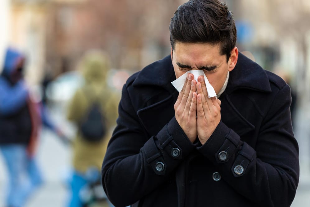 Junger Mann niest auf der Straße in ein Taschentuch: Die erhöhte Luftverschmutzung in Großstädten kann ein Auslöser für eine plötzliche Pollenallergie sein. Besonders die hohe Feinstaubbelastung setzt den Atemwegen zu.