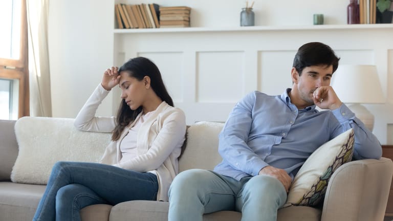 Paar sitzt distanziert voneinander auf dem Sofa:Über Blasenschwäche sollte offen mit dem Partner kommuniziert werden. Verschwiegenheit kann zu Distanz führen.