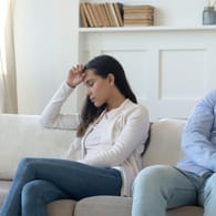 Paar sitzt distanziert voneinander auf dem Sofa:Über Blasenschwäche sollte offen mit dem Partner kommuniziert werden. Verschwiegenheit kann zu Distanz führen.