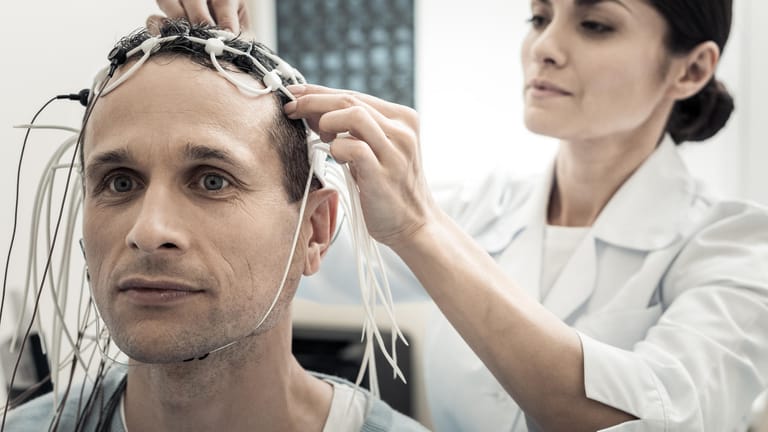 Eine Ärztin legt einem Patienten ein EEG an.