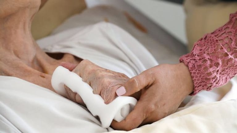 Eine Pflegeschwester hält die Hand einer alten Heimbewohnerin