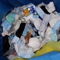 Corona Masken und Getränkeverpackungen in einem Abfallkorb (Symbolbild): Unbekannte haben medizinischen Sondermüll neben einer öffentlichen Mülltonne entsorgt.