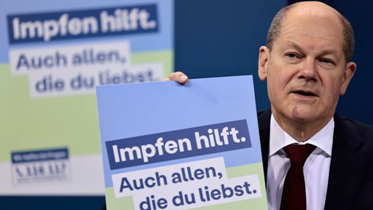 Bundeskanzler Olaf Scholz (SPD) präsentiert ein Plakat für eine neue Impfkampagne.