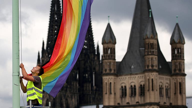 Ein Arbeiter hängt in Köln eine Regenbogenfahne auf (Archivbild): Mitarbeiter der katholischen Kirche haben sich jetzt öffentlich als queer bezeichnet.