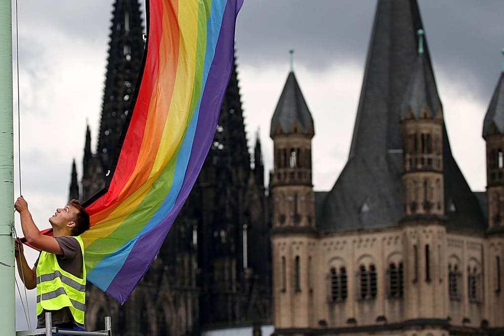 Ein Arbeiter hängt in Köln eine Regenbogenfahne auf (Archivbild): Mitarbeiter der katholischen Kirche haben sich jetzt öffentlich als queer bezeichnet.