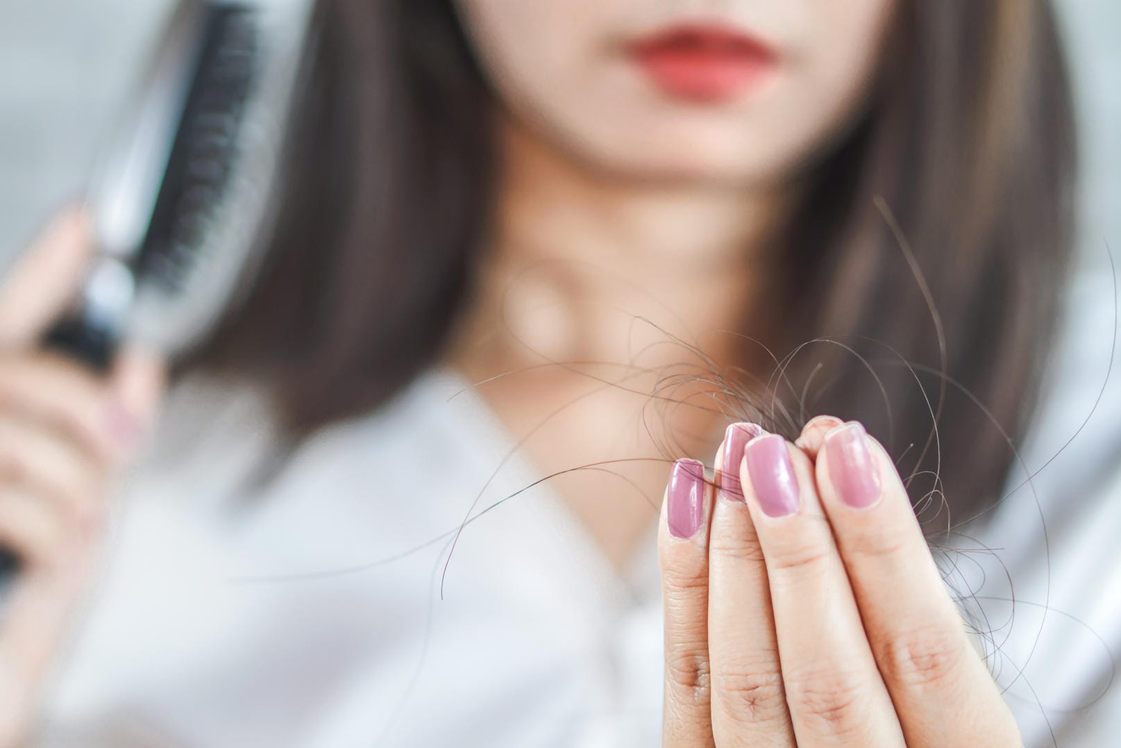 Frau hält Haare nach dem Bürsten in der Hand: Enorme Zugkräfte durch Frisuren oder aggressives Bürsten beanspruchen die Haarwurzeln und können zu Haarausfall führen.