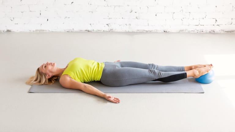Junge Frau liegt während Beckenbodenübung auf den Boden: Regelmäßiges Beckenbodentraining stärkt die Stützfunktion der Muskulatur und die Speicherfunktion der Blase.