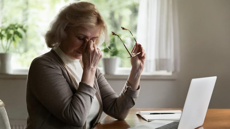 Ältere Dame vor Laptop ist müde: Schlafmangel wirkt sich auf die Leistungsfähigkeit des Gehirns aus. Als Folge können Konzentrationsstörungen auftreten.