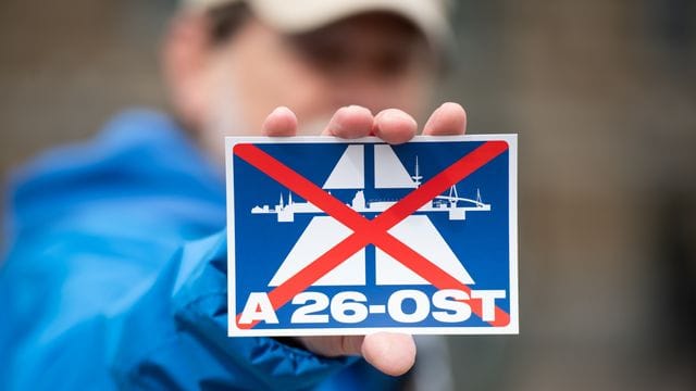 Ein Nabu-Aktivist hält während einer Demo einen Aufkleber mit dem durchgestrichenen Schriftzug "A26-OST" in der Hand (Archivbild): In zehn Jahren soll der Streckenabschnitt fertig gebaut sein. Ein Nabu-Aktivist hält während einer Demo einen Aufkleber mit dem durchgestrichenen Schriftzug "A26-OST" in der Hand (Archivbild): In zehn Jahren soll der Streckenabschnitt fertig gebaut sein.