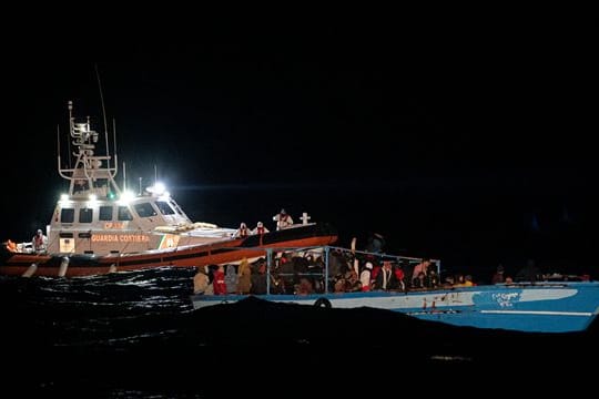 Ein Schiff der Küstenwache fährt zu dem völlig überfüllten Holzboot vor Lampedusa.