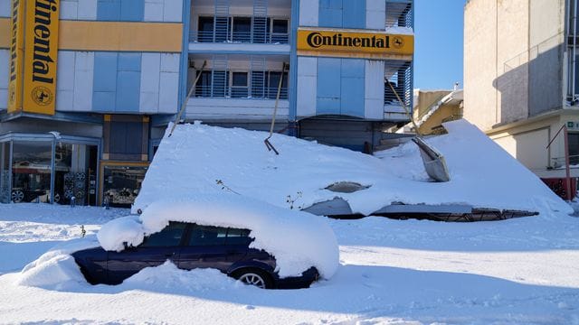 Ein schneebedecktes Auto steht vor einem beschädigten Gebäude. Ein schneebedecktes Auto steht vor einem beschädigten Gebäude.