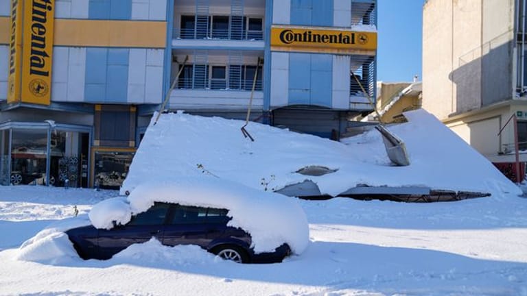 Ein schneebedecktes Auto steht vor einem beschädigten Gebäude.