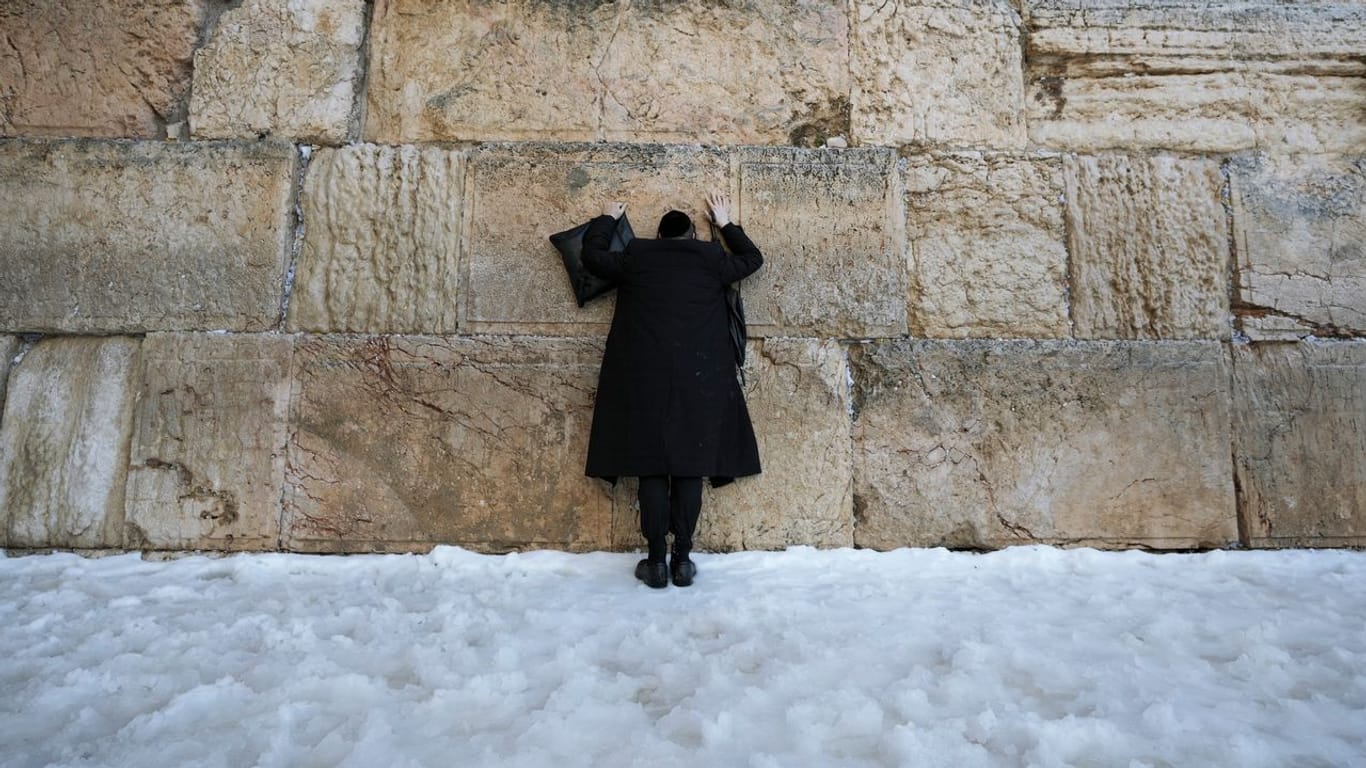 Ein ultra-orthodoxer jüdischer Mann steht im Schnee an der Klagemauer.
