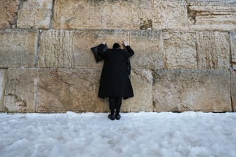 Ein ultra-orthodoxer jüdischer Mann steht im Schnee an der Klagemauer.