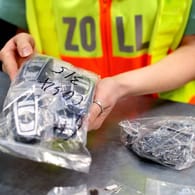 Eine Beamtin des deutschen Zoll eine Plastiktüte voller Mobiltelefone in den Händen (Archivbild): Beamte fanden eine Armbrust in einer Wohnung in Bergkamen.