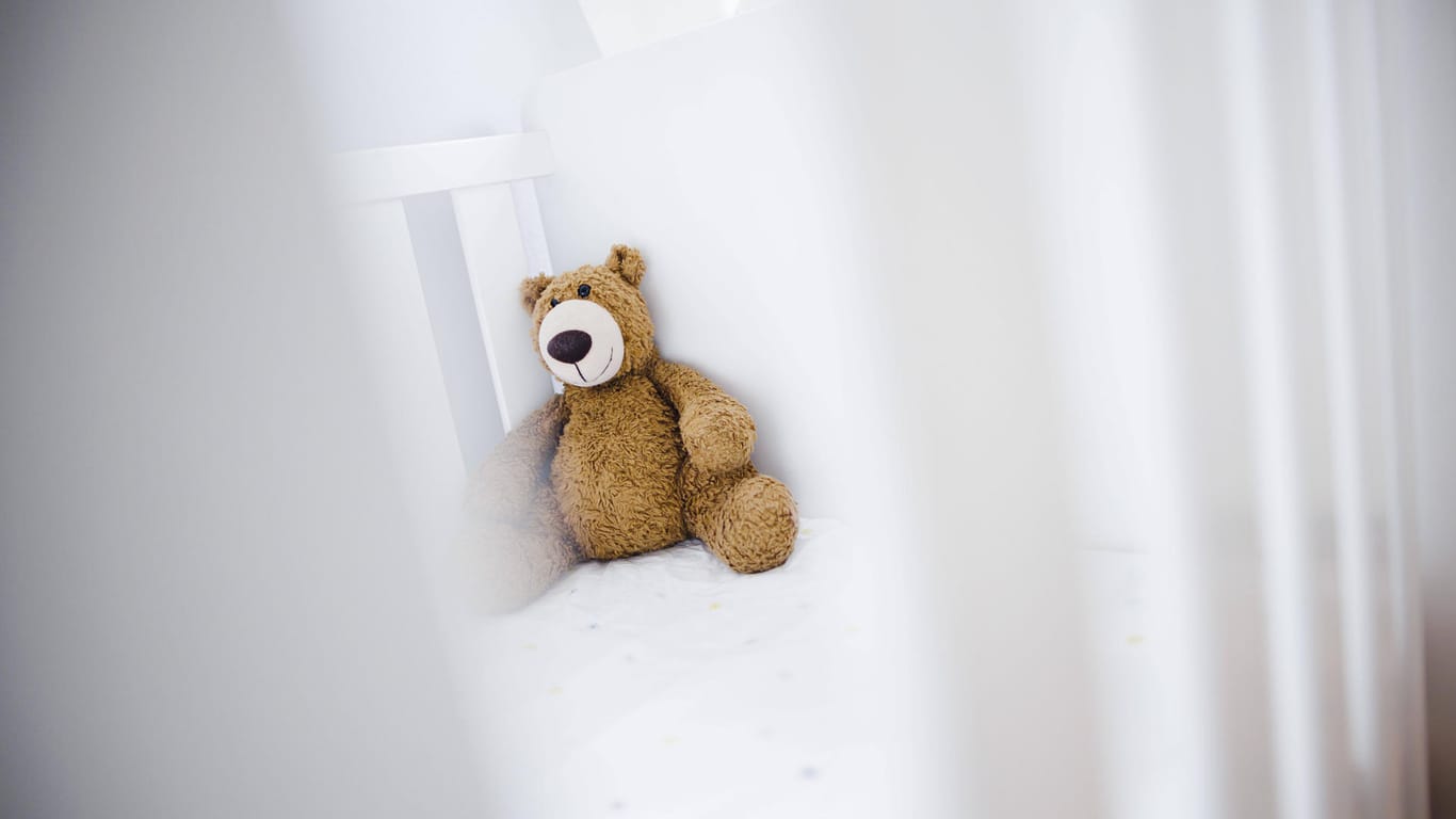 Ein Teddybär sitzt in einem Kinderbett (Symbolbild): Das Baby mit dem Namen Mia hatte es wohl besonders eilig, das Licht der Welt zu erblicken.