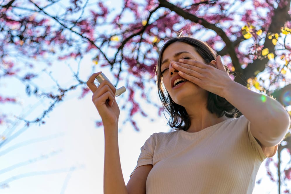 Junge Frau benutzt draußen Inhalator: Pollenallergiker haben sich an häufiges Niesen bereits gewöhnt. Bei Atemnot sollte allerdings ein Arzt aufgesucht werden.