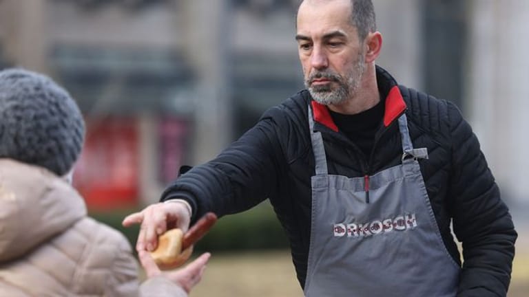Der bekannte Koch Volker Drkosch reicht ein Brötchen mit einer Bratwurst an eine bedürftige Frau.