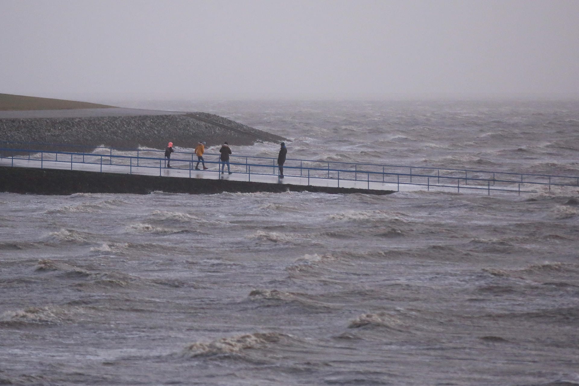 Besucher sind bei Sturm und Einbruch der Dunkelheit an der aufgewühlten Nordsee unterwegs