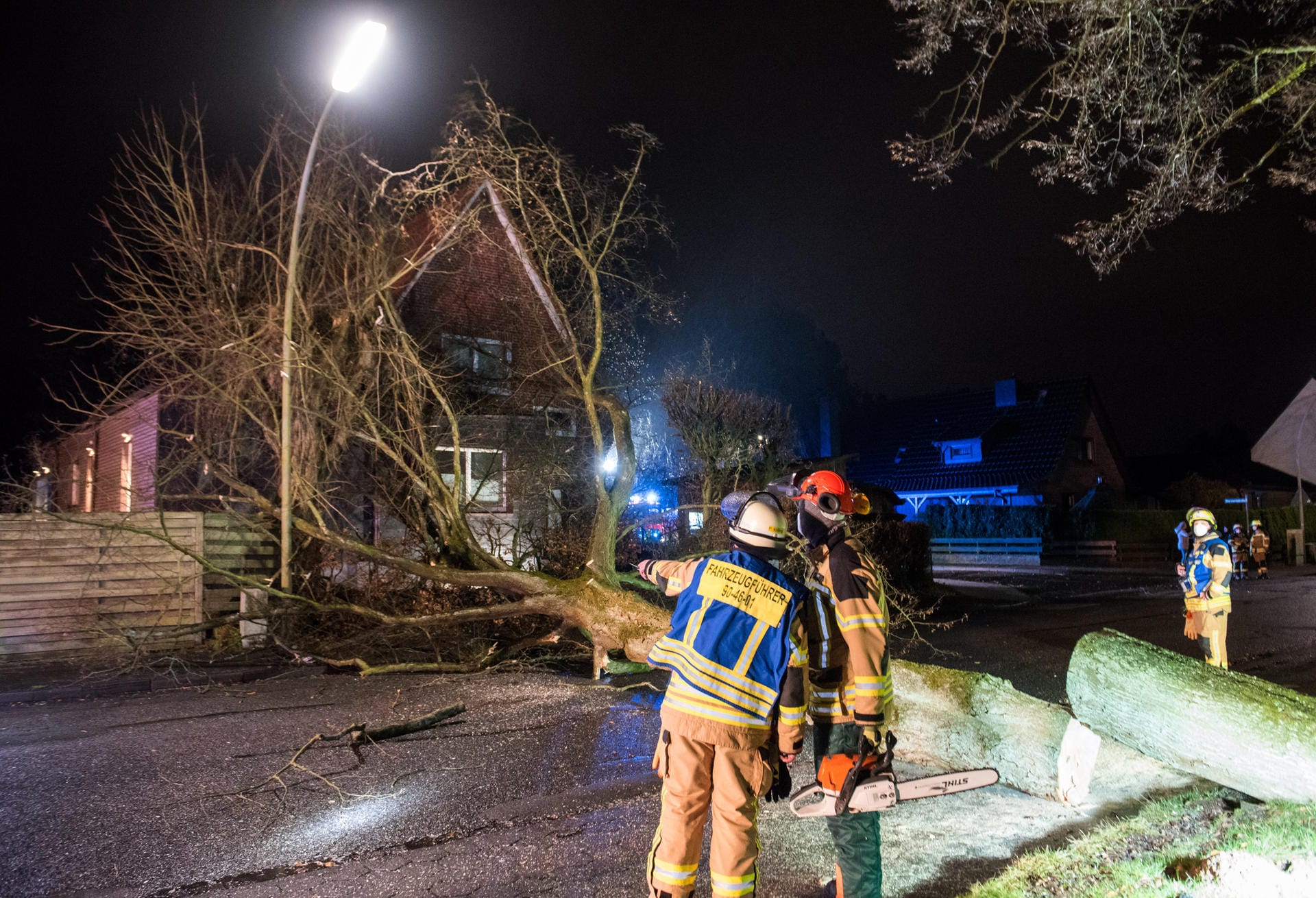Feuerwehrleute zersägen einen großen Baum, der auf ein Wohnhaus in Schleswig-Holstein gestürzt ist.
