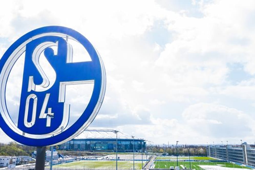 Im Vordergrund dreht sich das Logo des FC Schalke auf der Geschäftsstelle, im Hintergrund steht die Veltins Arena.