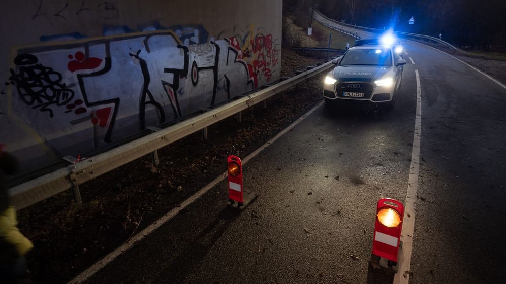 Ein Polizeiwagen steht an einer Absperrung an der Kreisstraße 22 rund einen Kilometer von dem Tatort entfernt.