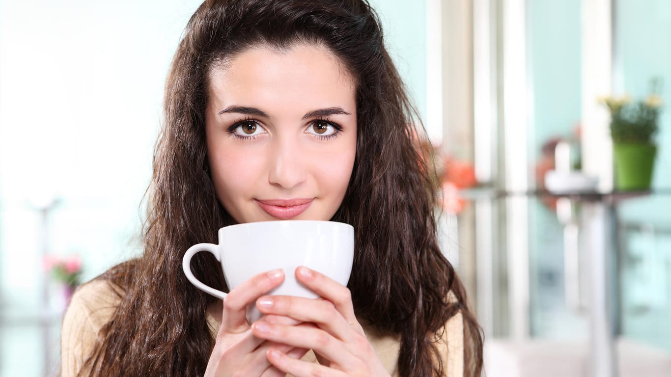 Eine Frau hält eine Tasse Kaffee in ihrer Hand: Viele Menschen trinken morgens einen Kaffee, um wach zu werden.