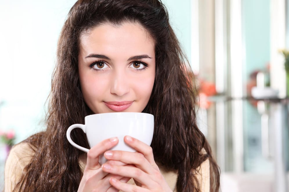 Eine Frau hält eine Tasse Kaffee in ihrer Hand: Viele Menschen trinken morgens einen Kaffee, um wach zu werden.