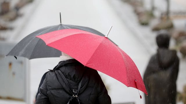 Passanten gehen mit Regenschirmen über eine Promenade