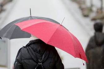 Passanten gehen mit Regenschirmen über eine Promenade