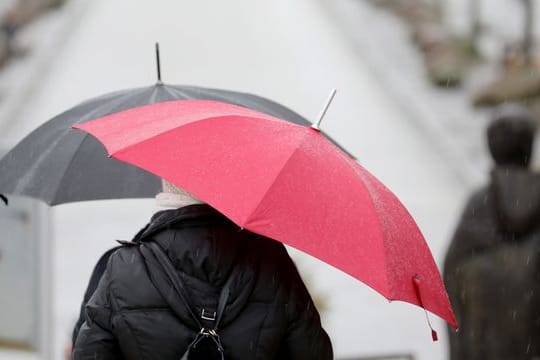 Passanten gehen mit Regenschirmen über eine Promenade