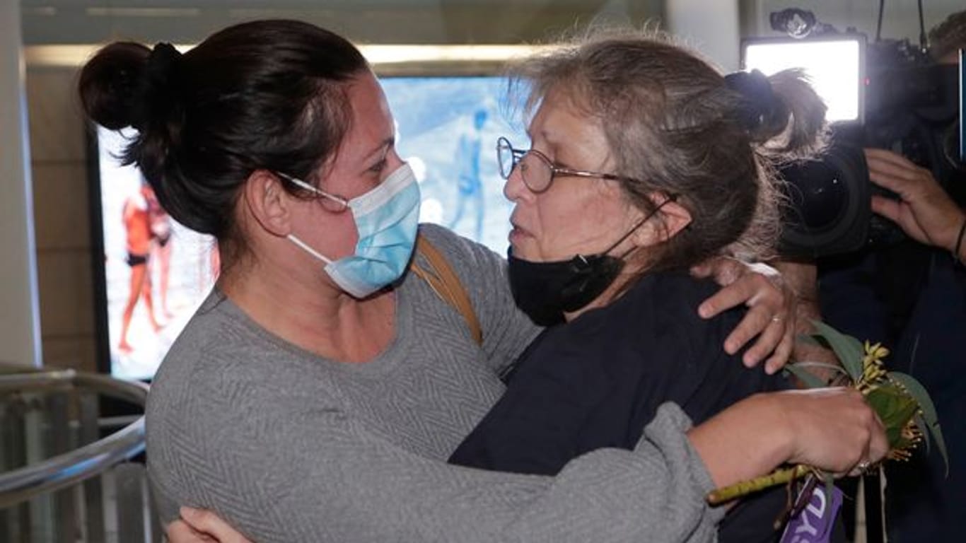 Eine Frau umarmt einem geliebten Menschen, nachdem sie mit einem Flug aus Los Angeles auf dem Flughafen von Sydney angekommen ist.