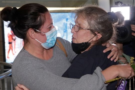 Eine Frau umarmt einem geliebten Menschen, nachdem sie mit einem Flug aus Los Angeles auf dem Flughafen von Sydney angekommen ist.