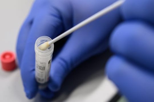 Ein Mann zeigt einen Abstrich: Die Inzidenz in Deutschland steigt seit mehreren Wochen.