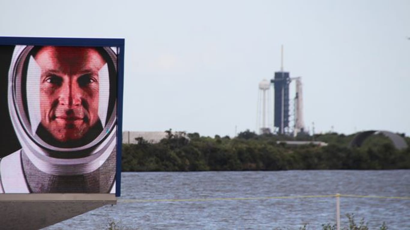 Matthias Maurer auf einem Video-Bildschirm vor dem Launchpad 39A in Cape Canaveral, an dem schon die Falcon-9-Rakete mit Crew Dragon-Kapsel aufgestellt ist.
