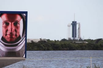 Matthias Maurer auf einem Video-Bildschirm vor dem Launchpad 39A in Cape Canaveral, an dem schon die Falcon-9-Rakete mit Crew Dragon-Kapsel aufgestellt ist.