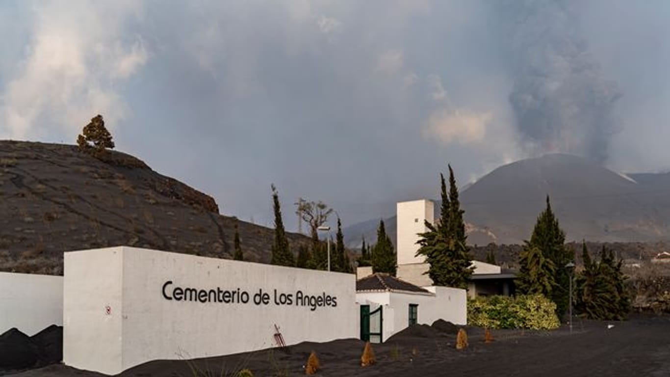 Der Friedhof von Los Angeles ist mit Asche bedeckt, während im Hintergrund die Rauch- und Aschesäule zu sehen ist, die der Vulkan Cumbre Vieja ausstößt.