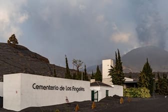 Der Friedhof von Los Angeles ist mit Asche bedeckt, während im Hintergrund die Rauch- und Aschesäule zu sehen ist, die der Vulkan Cumbre Vieja ausstößt.