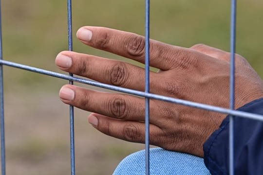 Die Hand eines Flüchtlings am Zaun einer Erstaufnahmeeinrichtung für Asylbewerber.