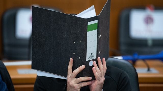 Der Angeklagte verbirgt sein Gesicht hinter einem Aktendeckel.