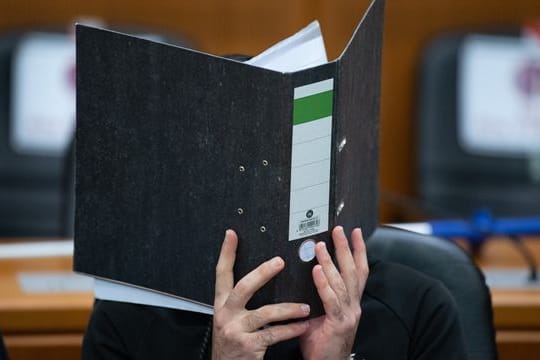 Der Angeklagte verbirgt sein Gesicht hinter einem Aktendeckel.