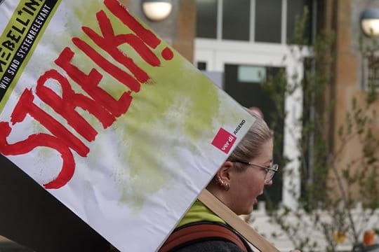 Eine Frau hält ein Schild hoch auf dem "Streik!" steht.