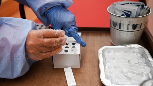 Eine Krankenschwester steckt während einer Corona-Testung ein Wattestäbchen in die Flüssigkeit eines Schnelltests. Eine Krankenschwester steckt während einer Corona-Testung ein Wattestäbchen in die Flüssigkeit eines Schnelltests.