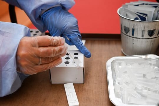 Eine Krankenschwester steckt während einer Corona-Testung ein Wattestäbchen in die Flüssigkeit eines Schnelltests.
