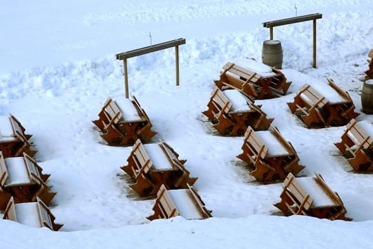 Schnee bedeckt Bänke und Tische an einer gesperrten Skipiste.