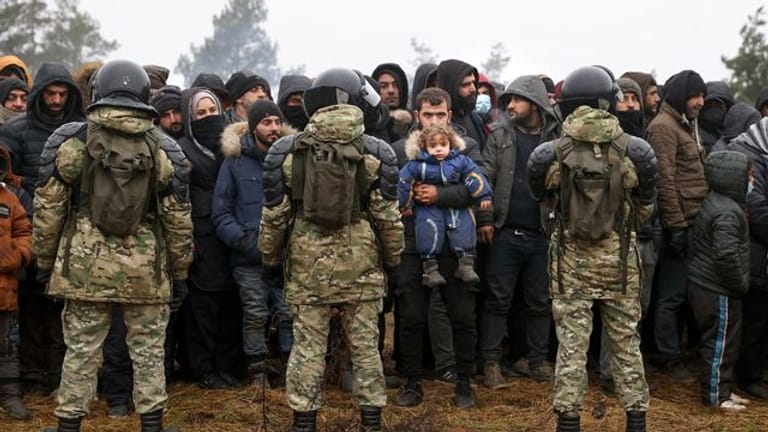 Migranten stehen an der belarussisch-polnischen Grenze vor belarussischen Soldaten.